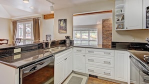 A kitchen with white cabinets, a granite countertop, a dishwasher, and a stone accent wall. - Private Mountain Town home Pet Friendly with Great Views - WD12 by Redawning (Copper Mountain)