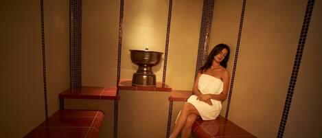 Une salle de spa avec un grand récipient en métal, des bancs rouges et un mur recouvert de carreaux.