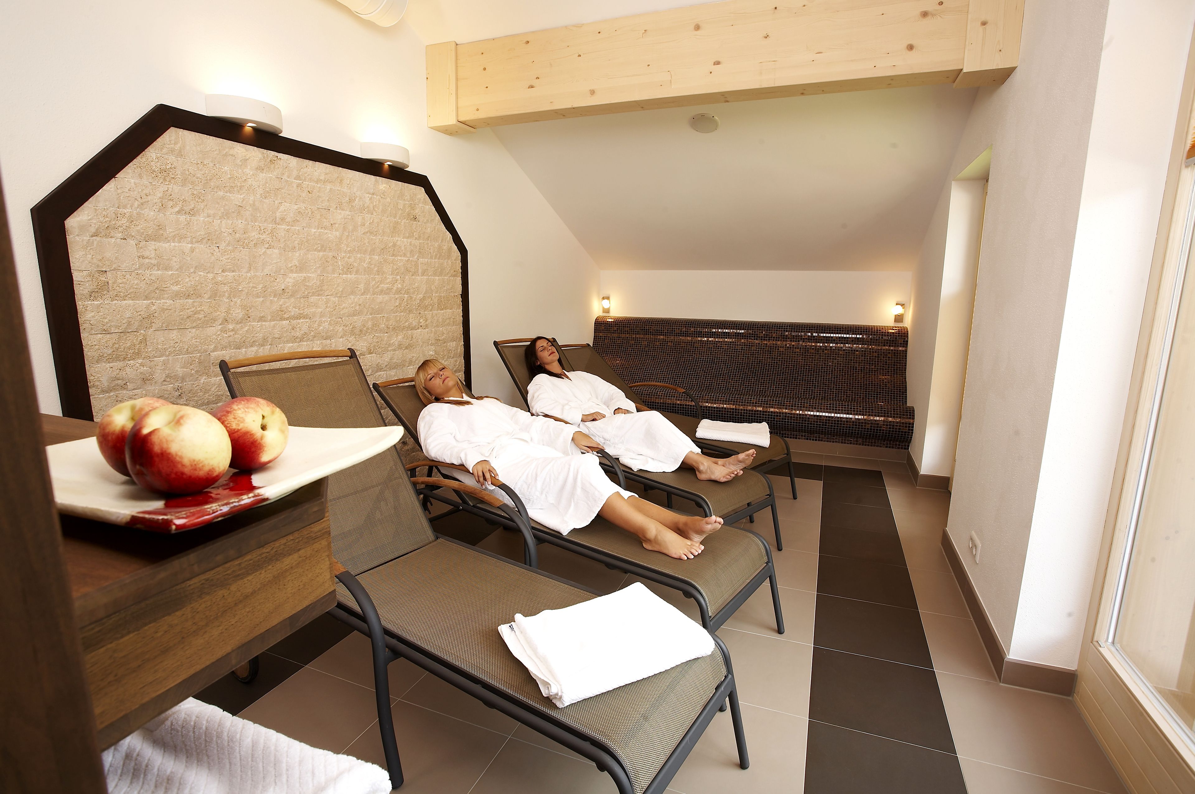 A room with two reclining chairs, a wooden table with apples, and a wall with a textured pattern.
