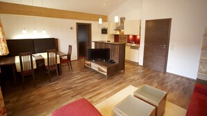 A modern living room with a wooden floor, a dining area with a table and chairs, a TV, and a kitchen area with cabinets and a stove. - Residenz Cristallo (Reit im Winkl)