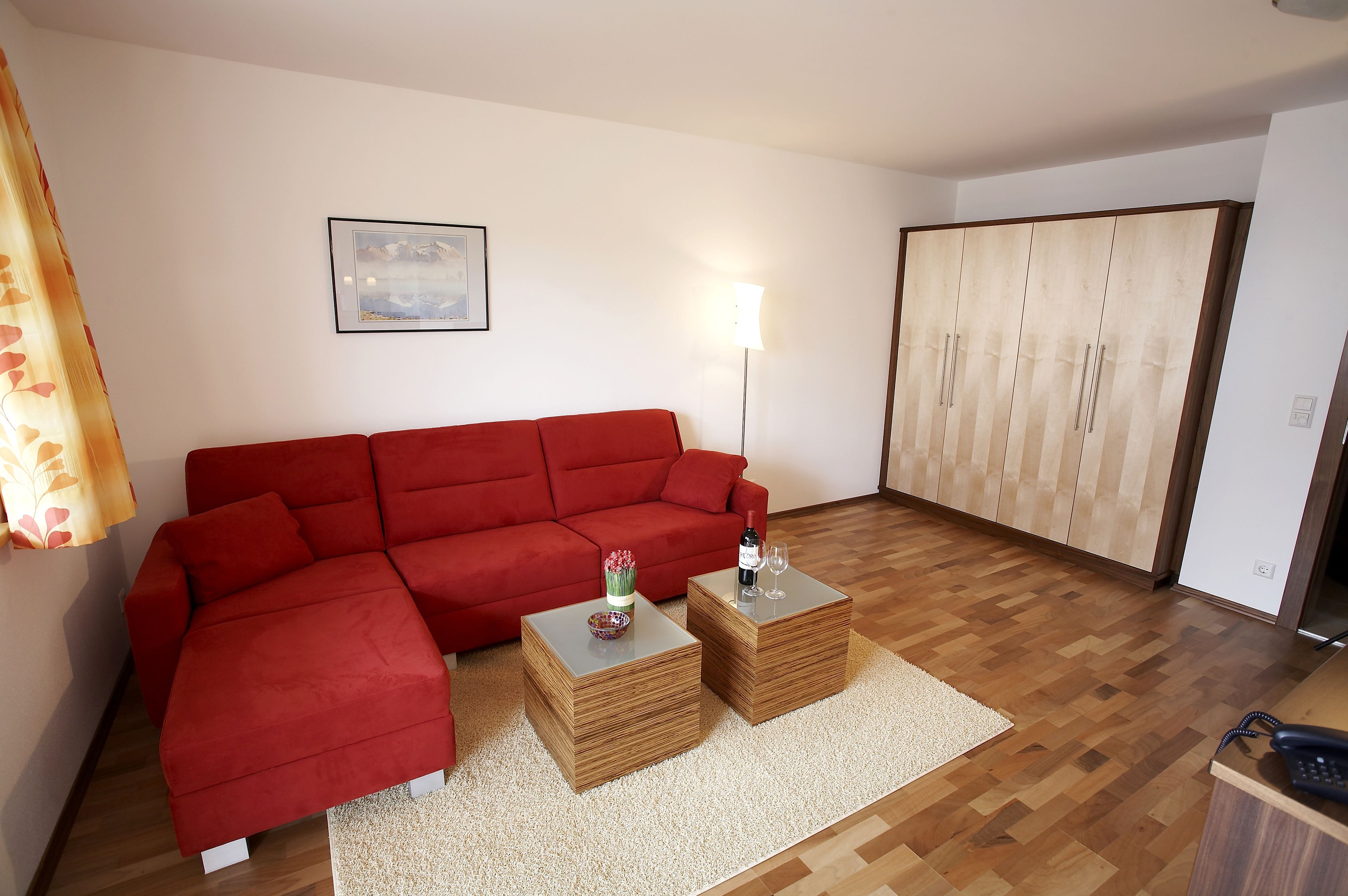 A living room with a red sofa, two wooden side tables, a lamp, and a wardrobe.