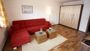 A living room with a red sofa, two wooden side tables, a lamp, and a wardrobe. - Residenz Cristallo (Reit im Winkl)