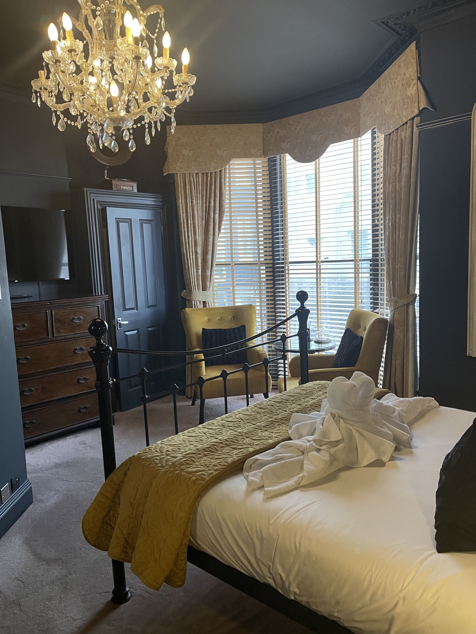 Une chambre à coucher avec un grand lit, un lustre, une armoire, une télévision et une fenêtre avec des rideaux.