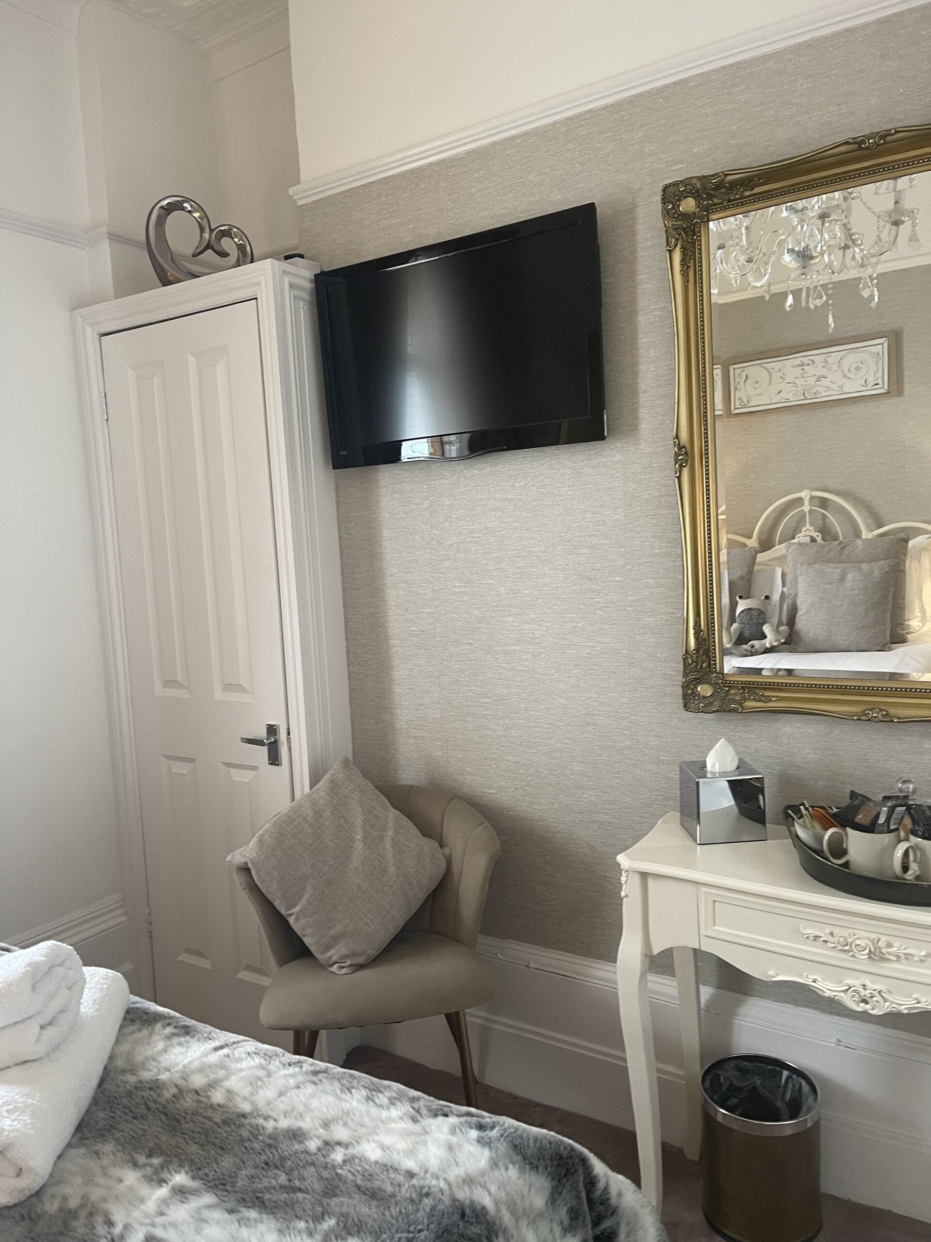 Une chambre à coucher comprenant un lit, une chaise, un bureau, un téléviseur, un miroir et une poubelle.