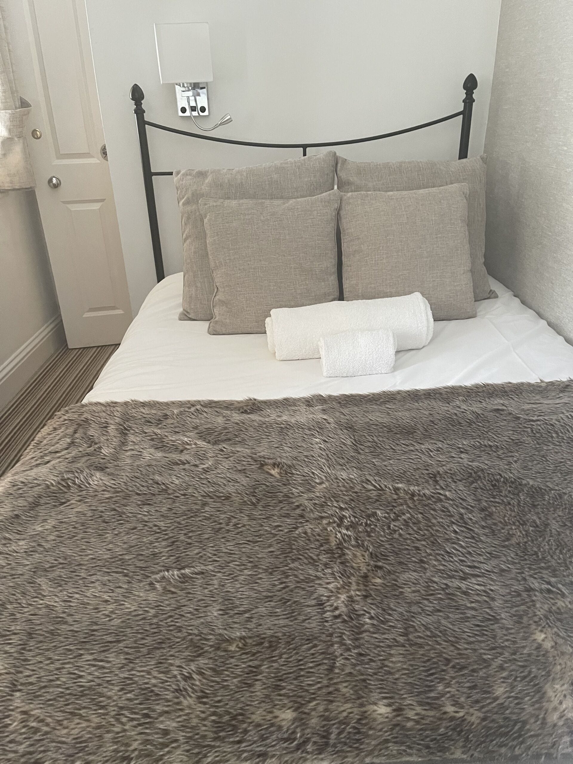 Una cama con un edredón gris esponjoso, dos almohadas y una toalla blanca enrollada.