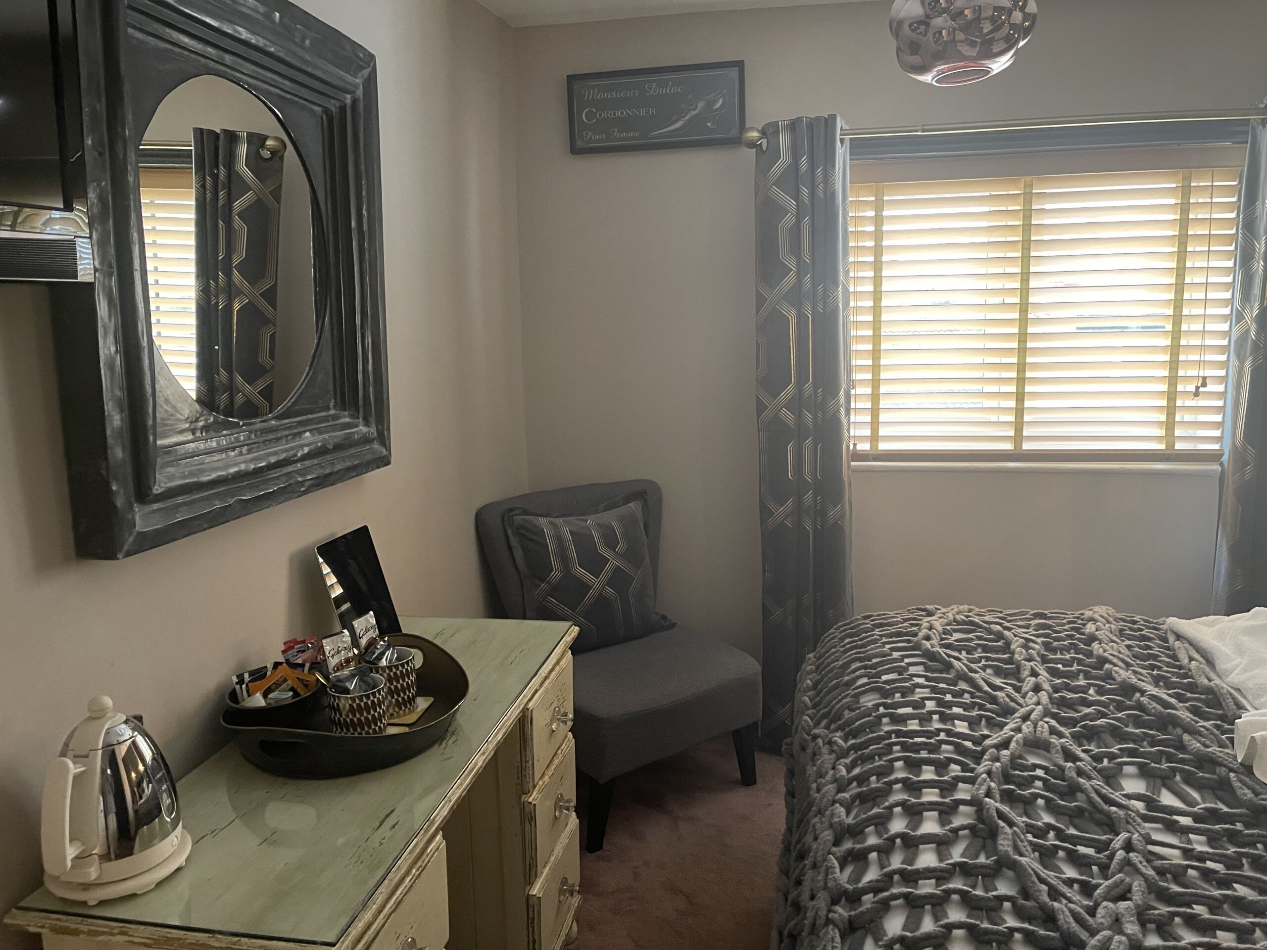 A bedroom with a bed, a dresser, a chair, a window with blinds, and a mirror.