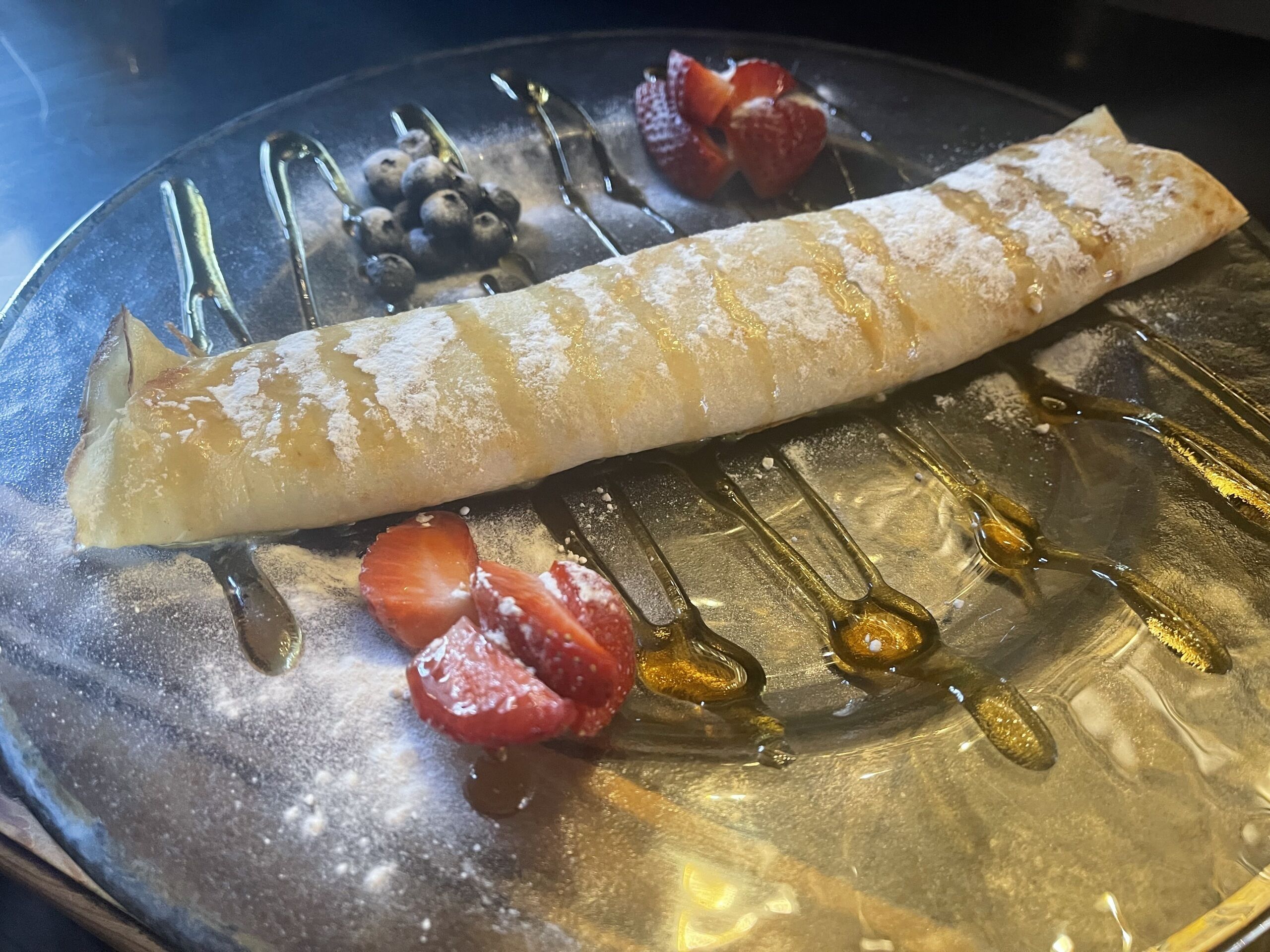 Crepe con azúcar glas y almíbar sobre un plato con fresas y arándanos.