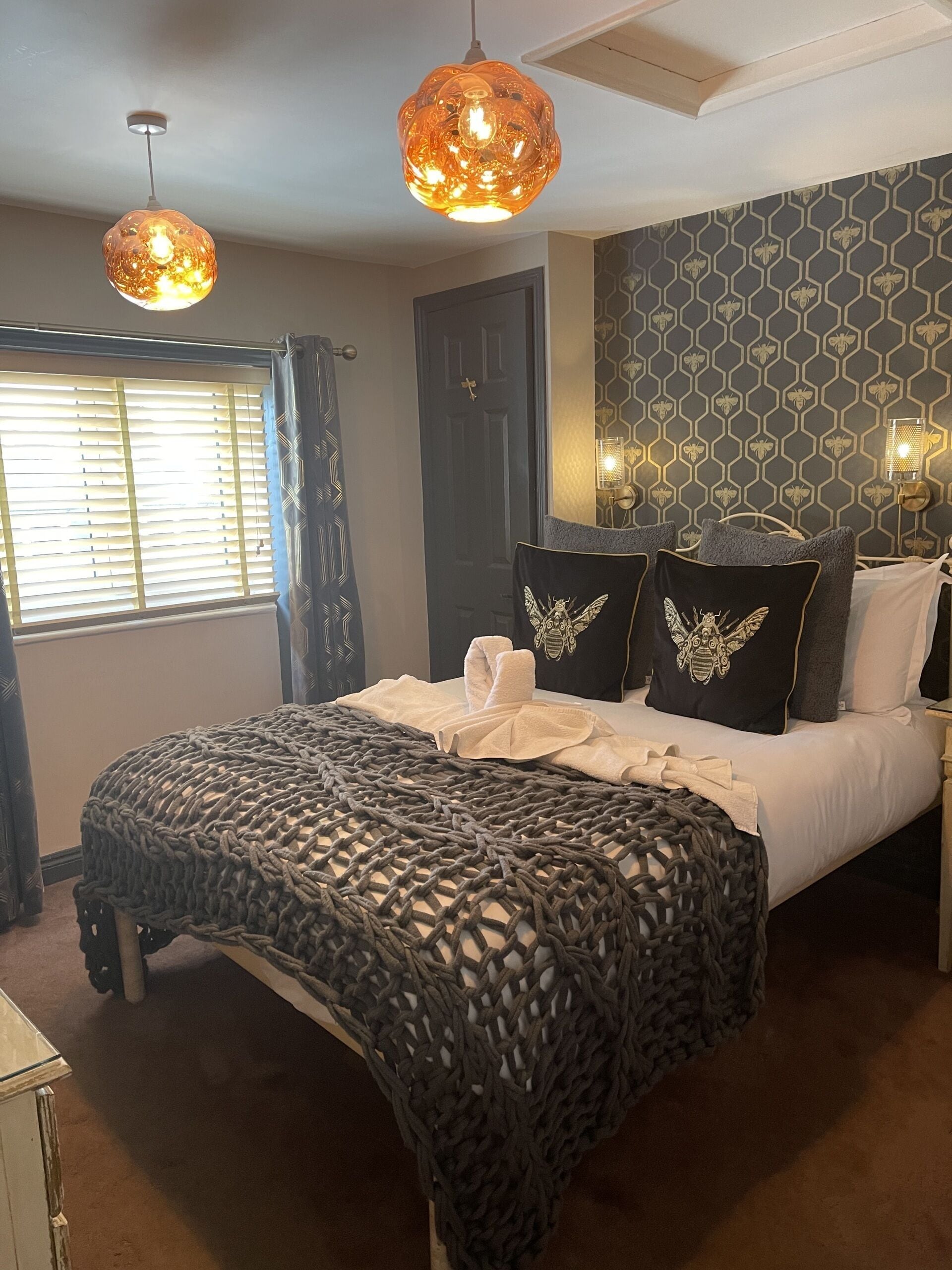 Un dormitorio con cama, un muro decorativo y dos lámparas colgantes.