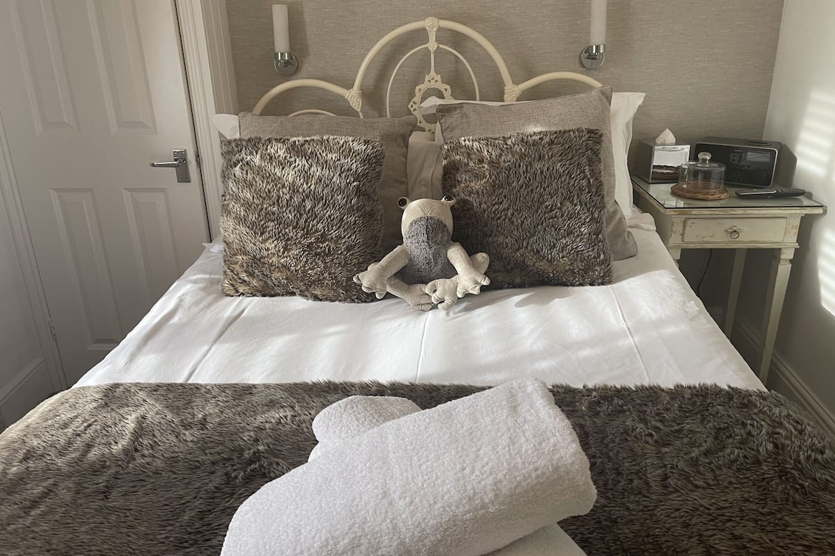 A bed with two fluffy pillows, a plush toy, and a white towel on a white bedspread.