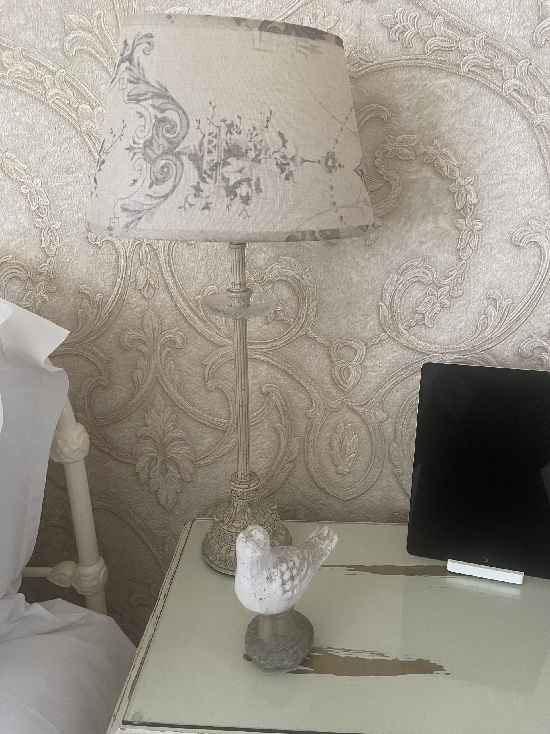 Une pièce avec une lampe décorative, une petite table ornée d’un objet décoratif et un lit avec un oreiller blanc.