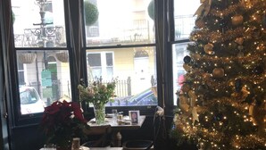 Un comedor con un árbol de Navidad, muebles de madera y vistas a la calle a través de amplias ventanas.