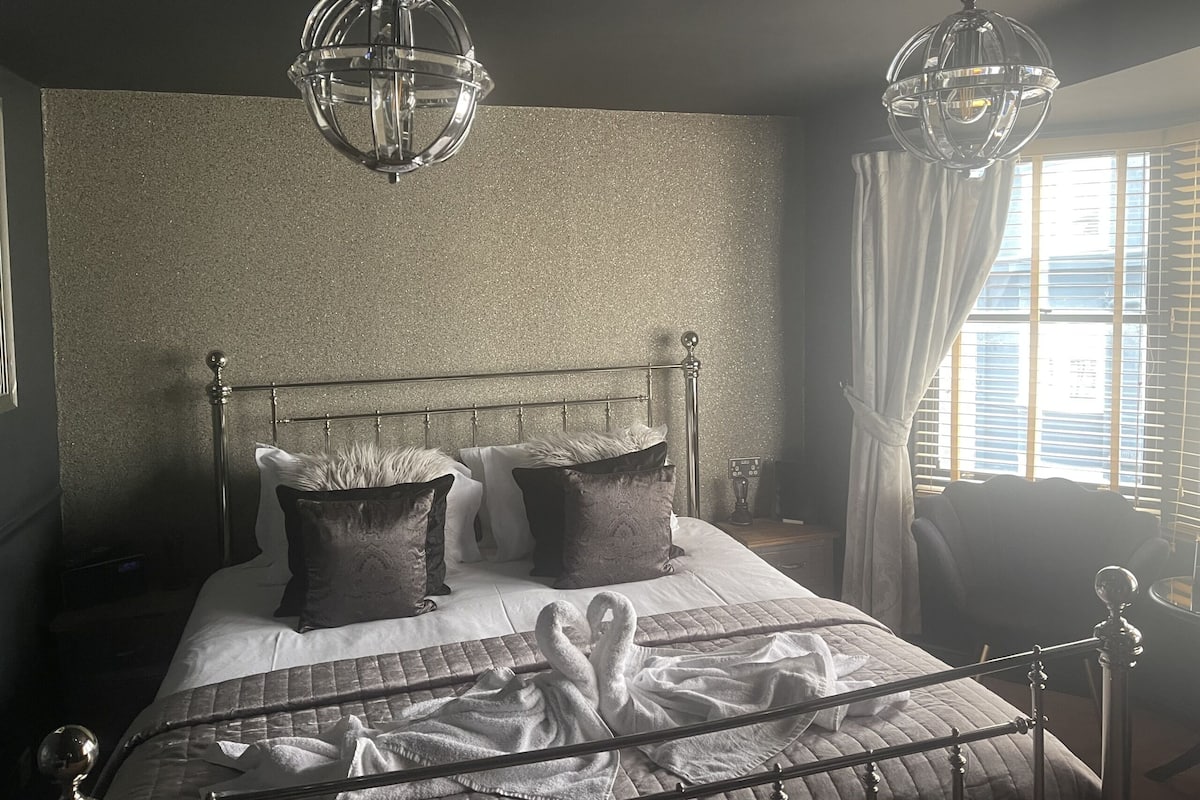 A bedroom with a metal bed frame, two large pillows, a quilted bedspread, and two hanging crystal chandeliers.