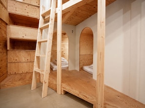 Une chambre à coucher aménagée dans les combles, avec une échelle, des étagères intégrées et un lit superposé.