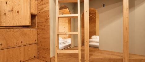 Habitación con literas, una escalera de madera, un armario pequeño y el número 8 en la pared.