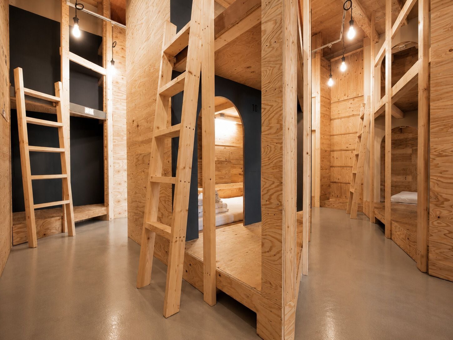A wooden interior with bunk beds, a ladder, and a dark wall.