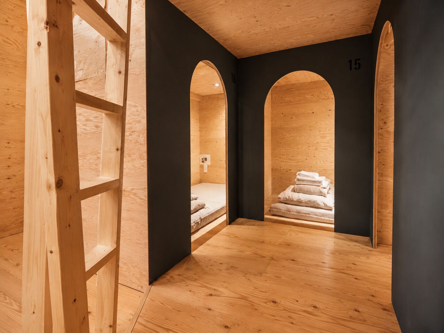 A room with a wooden floor, a bed, and a black wall with a number.