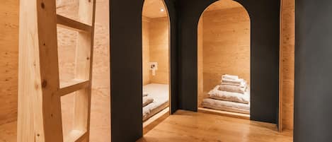 A room with a wooden floor, a bed, and a black wall with a number.