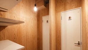 Un baño con paneles de madera, dos puertas blancas que indican 'TOILET' y un estante blanco.