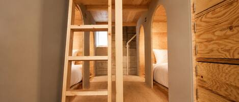 Quarto pequeno com beliches, escada de madeira e janela.