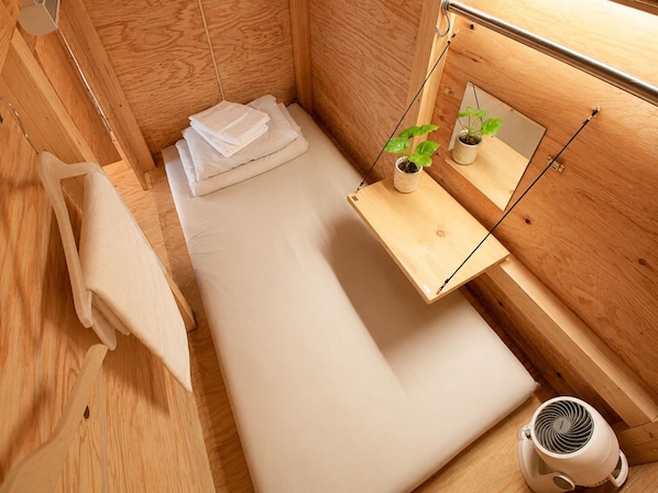 Habitación pequeña y acogedora, con muebles de madera, una cama, una mesita de noche con una planta, un espejo y un ventilador de pared.