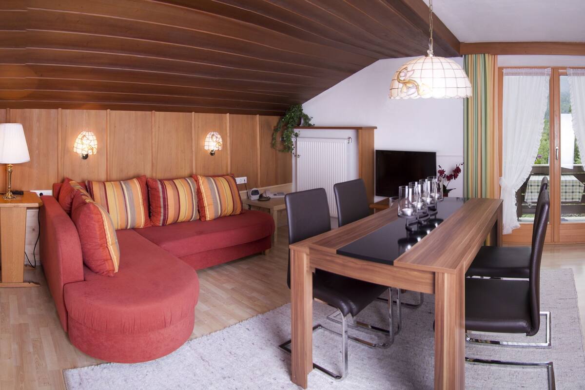 Uma sala de estar aconchegante com um sofá vermelho, mesa de jantar de madeira e uma televisão.