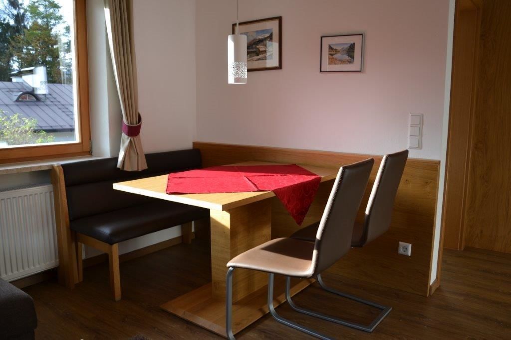Une petite pièce agréable, dotée d’une table et de chaises en bois, d’un banc et d’une fenêtre avec des rideaux.