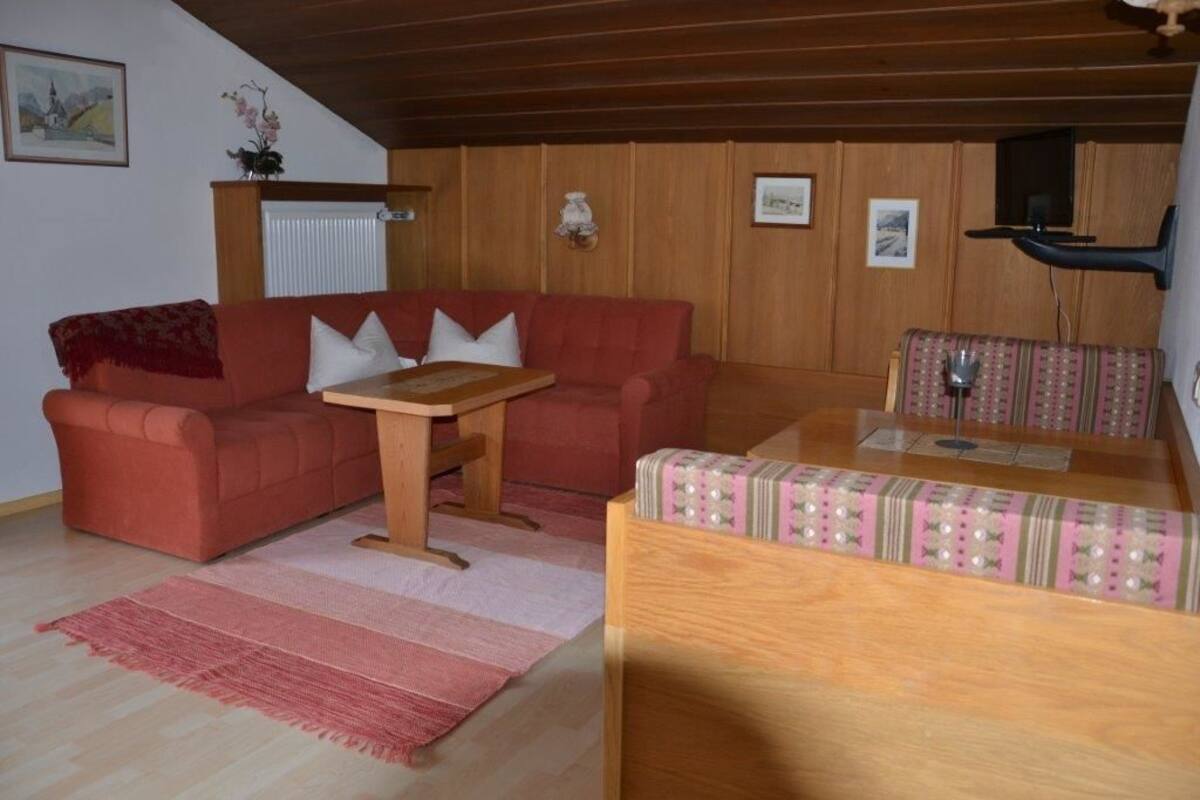 Uma sala de estar acolhedora com um sofá vermelho, uma mesa de centro de madeira e um banquinho estampado.
