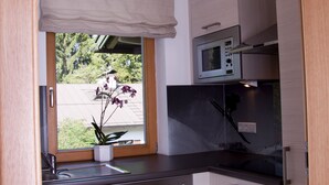 Uma cozinha compacta com micro-ondas, lava-louças e uma janela com vista para o verde.