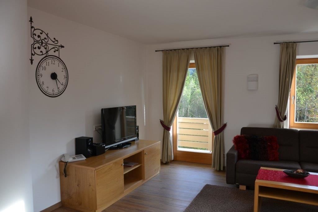 A living room with a wooden entertainment unit, a television, a sofa, and a window with curtains.