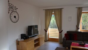 Uma sala de estar com um móvel de entretenimento em madeira, uma televisão, um sofá e uma janela com cortinas.