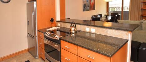 A modern kitchen with wooden cabinets, a stainless steel refrigerator, and a granite countertop.