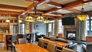A spacious kitchen with a stone fireplace, wooden beams, and a dining area with leather seating. - Luxury Suites At The Blackstone Mountain Lodge 1 Bedroom Condo (Canmore)