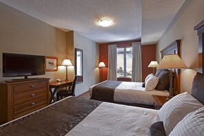 A hotel room with two beds, a desk with a flat-screen TV, and two lamps. - Luxury Suites At The Blackstone Mountain Lodge 1 Bedroom Condo (Canmore)