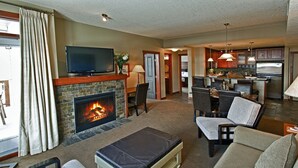 A living room with a fireplace, a television, and a dining area with chairs and a table. - Luxury Suites At The Blackstone Mountain Lodge 1 Bedroom Condo (Canmore)