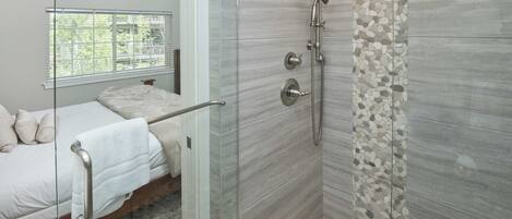 A modern bathroom with a glass shower enclosure, a bed with a white towel, and a window with blinds.
