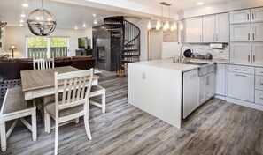 A modern kitchen with white cabinetry, a central island, and a dining area with a wooden table and chairs. - 9 Vail Rd. #26 3 Bedroom Condo by RedAwning (Vail)
