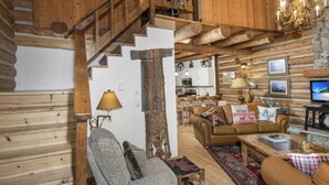A log cabin interior with a staircase, leather furniture, a chandelier, and a television. - Timbercreek #8b 2 Bedroom Home by RedAwning (Vail)