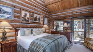 A log cabin bedroom with a large bed, two bedside lamps, a dresser, and framed pictures on the wall. - Timbercreek #8b 2 Bedroom Home by RedAwning (Vail)