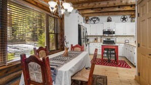 A wooden dining room with a table set for four, surrounded by chairs. A kitchen with white cabinets and a stove is visible in the background. - Timbercreek #8b 2 Bedroom Home by RedAwning (Vail)