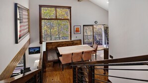 A dining area with a wooden table and bench, large windows with a view of trees, and a staircase with a railing. - Vail Point (Vail)