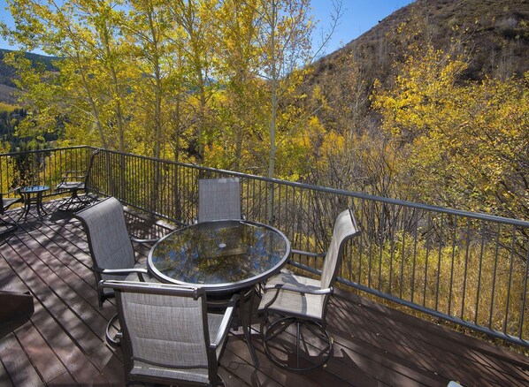 A deck with a round glass table and four chairs, surrounded by a metal railing, overlooking a forested hillside. - Vail Point (Vail)
