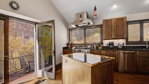 A modern kitchen with wooden cabinets, a central island, and a view of autumn trees through large windows. - Vail Point (Vail)