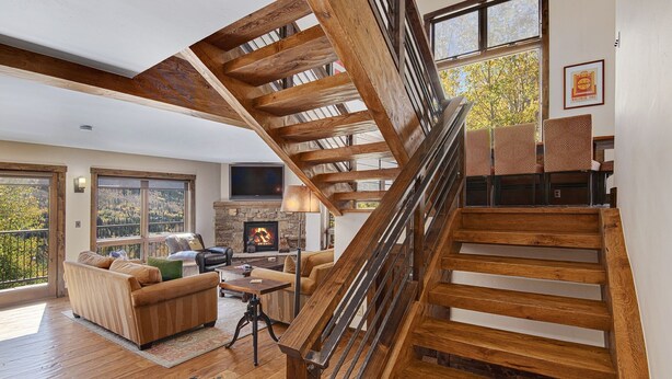 A spacious living room with a wooden staircase, a fireplace, and large windows offering a view of the outdoors. - Vail Point (Vail)