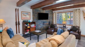 A cozy living room with a stone fireplace, a large TV, and a sofa with cushions. - Vantage Point 112 2 Bedroom Condo by RedAwning (Vail)