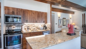 A modern kitchen with wooden cabinets, stainless steel appliances, a granite countertop, and a built-in island. - Vantage Point 112 2 Bedroom Condo by RedAwning (Vail)