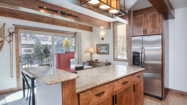 A kitchen with wooden cabinets, a stainless steel refrigerator, a granite countertop, and a window with blinds. - Vantage Point 112 2 Bedroom Condo by RedAwning (Vail)
