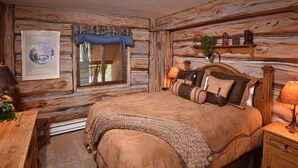 A log cabin-style bedroom with a large bed, wooden headboard, and a window with blinds.