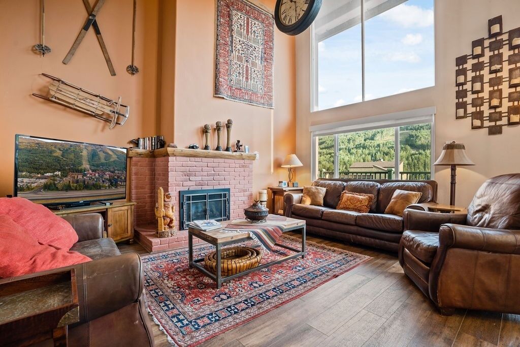A living room with a fireplace, leather furniture, a large window, and a television.