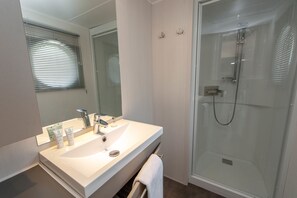 Un baño con lavamanos blanco, espejo y cabina de ducha con puertas de vidrio.