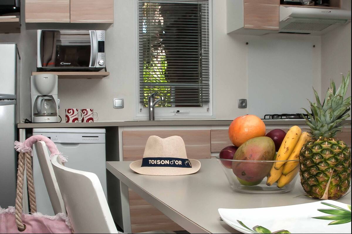 A kitchen with a microwave, coffee maker, and a fruit bowl containing a pineapple, mango, bananas, and oranges.